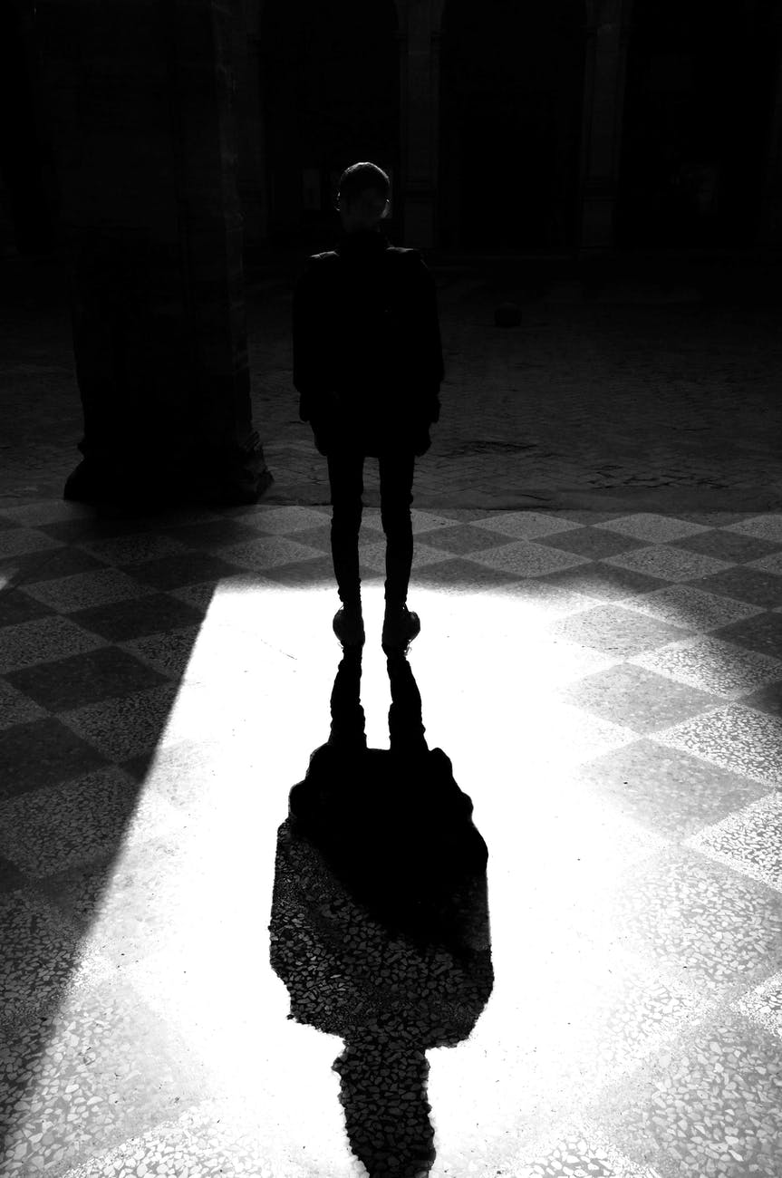 grayscale photography of man standing under the light